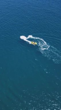 Yüksek hızda derin mavi denizde virajlar yaparken sarı sürat teknesinin yüzüşünü ve eğlenişini gösteren hava aracı görüntüsü. Yüksek kalite 4k dikey görüntü