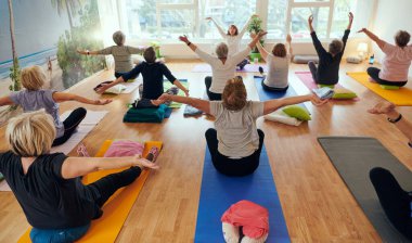 Bir grup son sınıf öğrencisi, güneş alan bir alanda eğitmenin rehberliğinde boyun, sırt ve bacak esnetme gibi çeşitli yoga egzersizleri yaparak refahı ve uyumu sağlıyorlar.. 