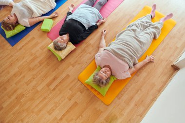 Üst düzey kadın grupları, güneş alan bir alanda eğitmenin rehberliğinde boyun, sırt ve bacak esnetme gibi çeşitli yoga egzersizlerine katılıyorlar, refah ve uyum sağlıyorlar.. 