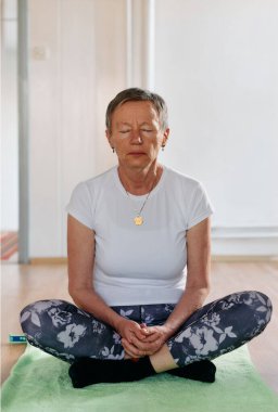 Bu güneşli ortamda, yaşlı bir kadın elleriyle çeşitli yoga pozisyonlarına giriyor, aktif yaşlanma, sağlık ve iç huzurun özünü somutlaştırıyor.. 
