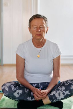 Bu güneşli ortamda, yaşlı bir kadın elleriyle çeşitli yoga pozisyonlarına giriyor, aktif yaşlanma, sağlık ve iç huzurun özünü somutlaştırıyor.. 