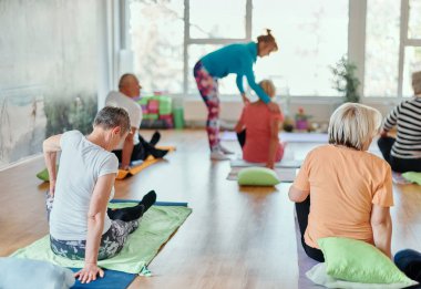 Bir grup son sınıf öğrencisi, güneş alan bir alanda eğitmenin rehberliğinde boyun, sırt ve bacak esnetme gibi çeşitli yoga egzersizleri yaparak refahı ve uyumu sağlıyorlar.. 