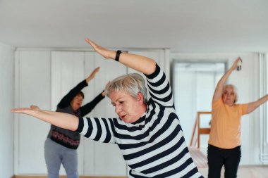Bir grup son sınıf öğrencisi, güneş alan bir alanda eğitmenin rehberliğinde boyun, sırt ve bacak esnetme gibi çeşitli yoga egzersizleri yaparak refahı ve uyumu sağlıyorlar.. 