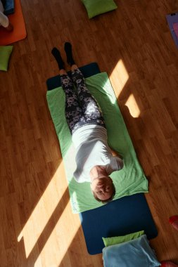 Yaşlı bir kadın yerde esneme ve meditasyon seansı yapar, hizalama ve dikkatli rahatlama üzerine yoğunlaşır..