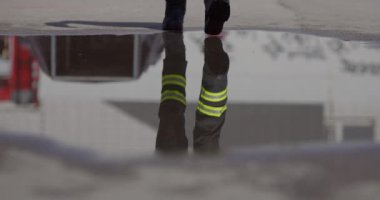 Yansıtıcı sahne, tehlikeli bir itfaiye görevine giden bir itfaiyeciyi yakalıyor. Yüzündeki cesaret ve hazırlığı simgeleyen bir yangın hortumunu tutarken görüntüsü su yüzeyinde yansıtılıyor.
