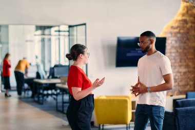 Young business colleagues, including an African American businessman, engage in a conversation about business issues in the hallway of a modern startup coworking center clipart