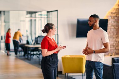 Young business colleagues, including an African American businessman, engage in a conversation about business issues in the hallway of a modern startup coworking center clipart