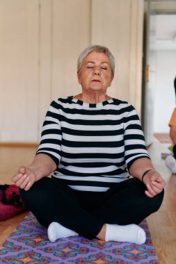 Bu güneşli ortamda, yaşlı bir kadın elleriyle çeşitli yoga pozisyonlarına giriyor, aktif yaşlanma, sağlık ve iç huzurun özünü somutlaştırıyor.. 