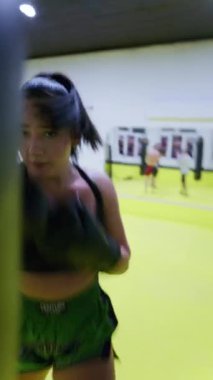 Kickboks yapan kadın boksör yumruklarını çalıştırırken kız hızlı saldırırken spor salonunda günlük antrenman yapıyor. Yüksek kalite 8K görüntü