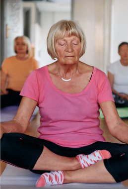 Bu güneşli ortamda, yaşlı bir kadın elleriyle çeşitli yoga pozisyonlarına giriyor, aktif yaşlanma, sağlık ve iç huzurun özünü somutlaştırıyor.. 