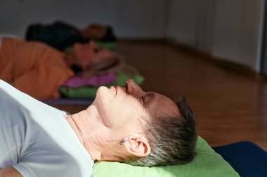 Yaşlı bir kadın yerde esneme ve meditasyon seansı yapar, hizalama ve dikkatli rahatlama üzerine yoğunlaşır..