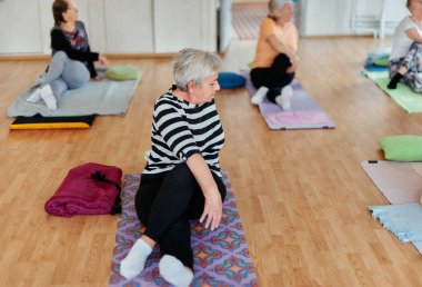Bir grup son sınıf öğrencisi, güneş alan bir alanda eğitmenin rehberliğinde boyun, sırt ve bacak esnetme gibi çeşitli yoga egzersizleri yaparak refahı ve uyumu sağlıyorlar.. 