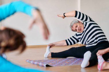 Bir grup son sınıf öğrencisi, güneş alan bir alanda eğitmenin rehberliğinde boyun, sırt ve bacak esnetme gibi çeşitli yoga egzersizleri yaparak refahı ve uyumu sağlıyorlar.. 