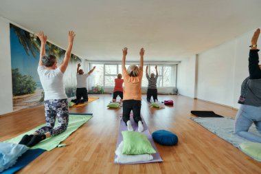 Bir grup son sınıf öğrencisi, güneş alan bir alanda eğitmenin rehberliğinde boyun, sırt ve bacak esnetme gibi çeşitli yoga egzersizleri yaparak refahı ve uyumu sağlıyorlar.. 