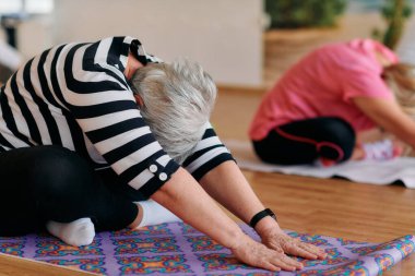 Bir grup son sınıf öğrencisi, güneş alan bir alanda eğitmenin rehberliğinde boyun, sırt ve bacak esnetme gibi çeşitli yoga egzersizleri yaparak refahı ve uyumu sağlıyorlar.. 