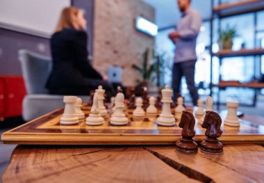 A close up of chess pieces on a board highlights the parallels between strategy and business, while a team collaborates in the background on their own tactical discussions. clipart