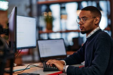 Yetenekli bir Afrikalı Amerikalı programcı, modern bir ofiste bilgisayarının başına oturmuş, problem çözme ve teknoloji konusundaki uzmanlığını sergiliyor..