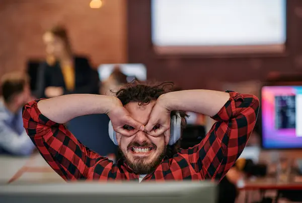 stock image A cheerful man in a coworking space engages in a lively video call, showcasing his excitement and creativity through playful hand gestures.