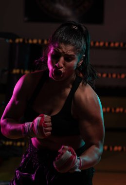 Kadın Latin boksör elleri bandajlı spor salonunda antrenman yapıyor yumruk atıyor ve ciddi bir ifadeyle kameraya bakıyor.. 