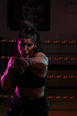 Kadın Latin boksör elleri bandajlı spor salonunda antrenman yapıyor yumruk atıyor ve ciddi bir ifadeyle kameraya bakıyor.. 
