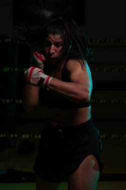 Kadın Latin boksör elleri bandajlı spor salonunda antrenman yapıyor yumruk atıyor ve ciddi bir ifadeyle kameraya bakıyor.. 