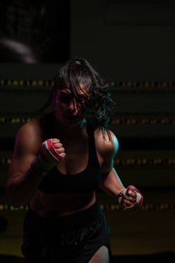 Kadın Latin boksör elleri bandajlı spor salonunda antrenman yapıyor yumruk atıyor ve ciddi bir ifadeyle kameraya bakıyor.. 