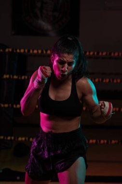 Kadın Latin boksör elleri bandajlı spor salonunda antrenman yapıyor yumruk atıyor ve ciddi bir ifadeyle kameraya bakıyor.. 
