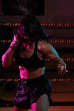 Kadın Latin boksör elleri bandajlı spor salonunda antrenman yapıyor yumruk atıyor ve ciddi bir ifadeyle kameraya bakıyor.. 