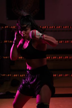 Kadın Latin boksör elleri bandajlı spor salonunda antrenman yapıyor yumruk atıyor ve ciddi bir ifadeyle kameraya bakıyor.. 