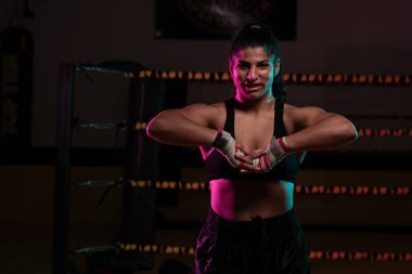 Kadın Latin boksör elleri bandajlı spor salonunda antrenman yapıyor yumruk atıyor ve ciddi bir ifadeyle kameraya bakıyor.. 