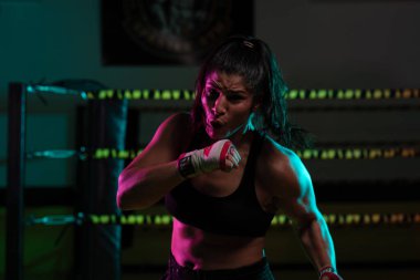Kadın Latin boksör elleri bandajlı spor salonunda antrenman yapıyor yumruk atıyor ve ciddi bir ifadeyle kameraya bakıyor.. 