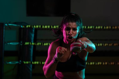 Kadın Latin boksör elleri bandajlı spor salonunda antrenman yapıyor yumruk atıyor ve ciddi bir ifadeyle kameraya bakıyor.. 