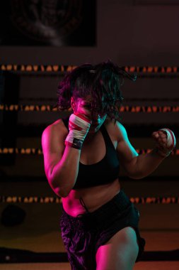 Kadın Latin boksör elleri bandajlı spor salonunda antrenman yapıyor yumruk atıyor ve ciddi bir ifadeyle kameraya bakıyor.. 
