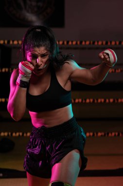 Kadın Latin boksör elleri bandajlı spor salonunda antrenman yapıyor yumruk atıyor ve ciddi bir ifadeyle kameraya bakıyor.. 
