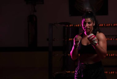 Kadın Latin boksör elleri bandajlı spor salonunda antrenman yapıyor yumruk atıyor ve ciddi bir ifadeyle kameraya bakıyor.. 