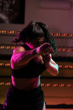Kadın Latin boksör elleri bandajlı spor salonunda antrenman yapıyor yumruk atıyor ve ciddi bir ifadeyle kameraya bakıyor.. 