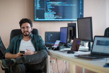 Bir programcı ofisinde otururken akıllı telefon uygulamalarını özenle test eder.