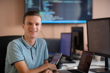 Genç bir programcı ofisinde masasında oturmuş, akıllı telefonlar için yenilikçi yeni uygulamaları test etmeye odaklanmış, yaratıcılık ve teknoloji ruhunu somutlaştırıyor..
