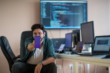 Bir programcı ofisinde otururken akıllı telefon uygulamalarını özenle test eder.