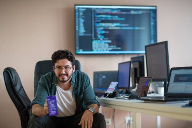 Bir programcı ofisinde otururken akıllı telefon uygulamalarını özenle test eder.