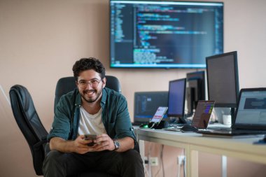 Bir programcı ofisinde otururken akıllı telefon uygulamalarını özenle test eder.