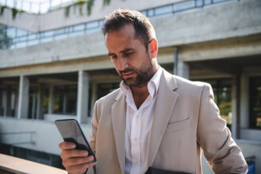 Akıllı telefonunu açık havada kullanan bir işadamı modern profesyonel hayatta teknolojinin ve hareketliliğin kusursuz bütünlüğünü sergiliyor.