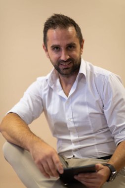 Güvenilir bir iş adamı oturmuş ve kararlı bir ifadeyle dizüstü bilgisayar kullanırken, bej bir arka plan profesyonel atmosferi yükselterek üretkenliğini ve uzmanlığını sergiliyor.
