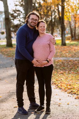 A man lovingly embraces his pregnant wife in the park, sharing a peaceful moment of warmth and affection. clipart