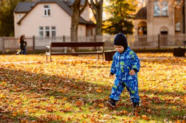 A joyful little boy in his winter coat and hat plays happily in the park, surrounded by the love and warmth of his smiling parents. clipart