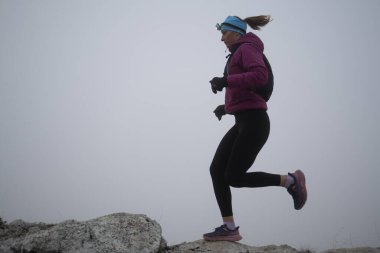 Gökyüzü koşuyor ya da bir dağın tepesinde egzersiz yapan bir kadını takip ediyor. Açık havada antrenman yapan koşucu bir kadın aktif ve zinde bir hayat sürüyor. Siluet sabahın erken saatlerinde.
