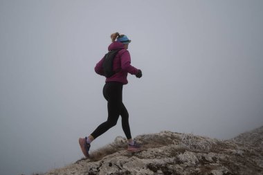 Gökyüzü koşuyor ya da bir dağın tepesinde egzersiz yapan bir kadını takip ediyor. Açık havada antrenman yapan koşucu bir kadın aktif ve zinde bir hayat sürüyor. Siluet sabahın erken saatlerinde.