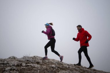 Sabahın erken saatlerinde dağın tepesinde koşan atlet çift patikası. Gökyüzü koşma konsepti, arka planda gökyüzü varken sınırda koşmak tehlikeli. Sağlıklı yaşam, kardiyo egzersizi, spor.