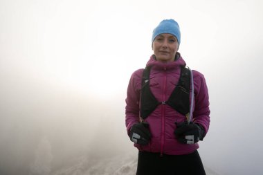 Kadın yürüyüşçü ya da triatlon patika koşucusu gün batımında sisle dağlarda bir patikada portre çiziyor.