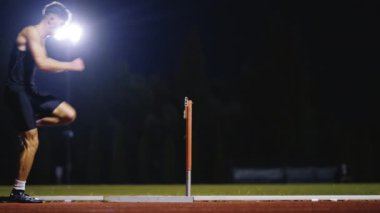 Güçlü Erkek Sporcu bir engele doğru koşuyor, bir yarışta koşarken bariyerin üzerinden yüksek hızda atlıyor. Hız Rampası Efektli Süper Yavaş Sinema Görüntüsü.